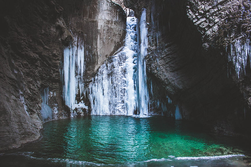 Frozen waterfall in cave with turquoise pool