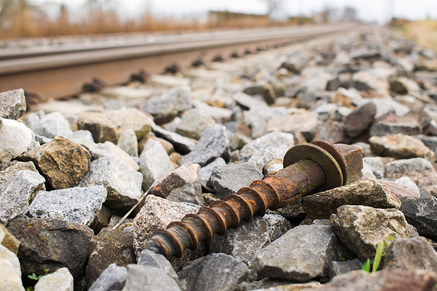 Rusty railway screw on gravel ballast near train tracks