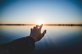 Hand Reaching for Sun Over Calm Water Horizon