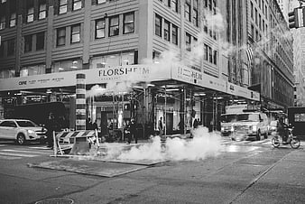 Black and white urban street scene with steam rising from manhole