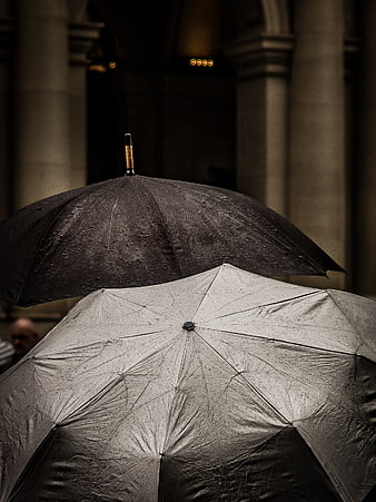 Two wet umbrellas in rain against blurred architecture