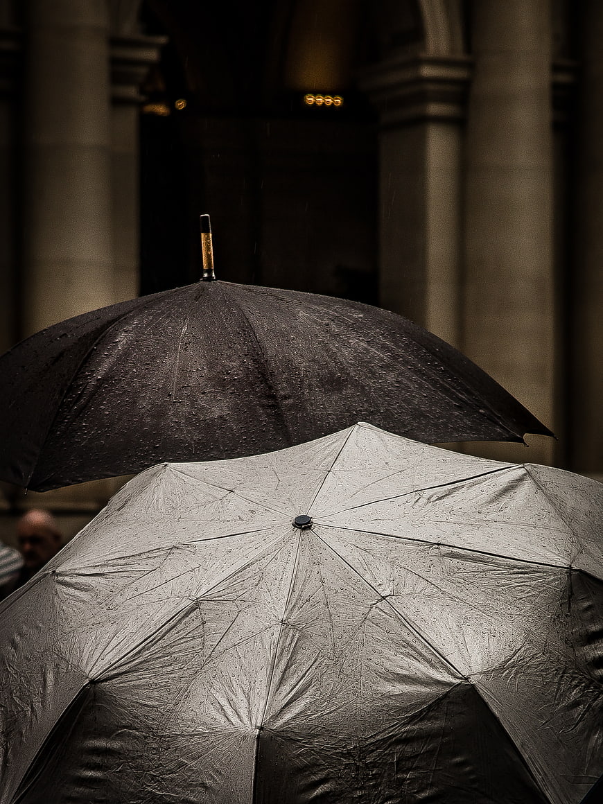 Two wet umbrellas in rain against blurred architecture