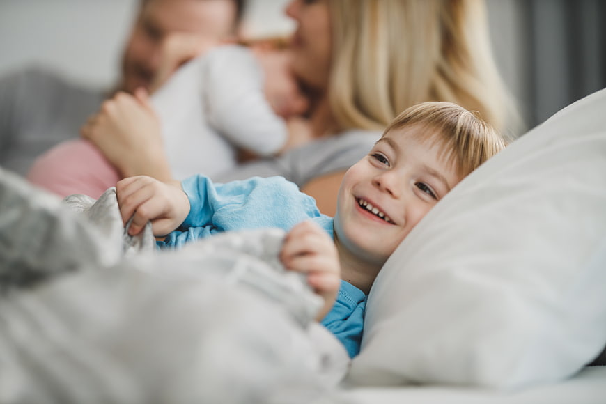 Happy Boy Smiling in Bed with Parents in Background