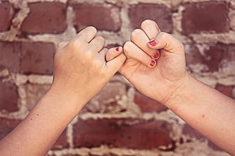 Two hands making pinky promise against brick wall