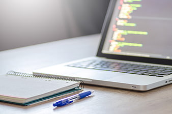 Laptop with Code and Notebook on Wooden Desk