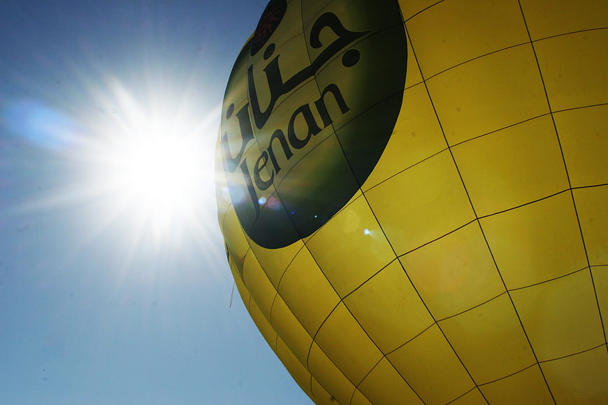 Yellow Hot Air Balloon with Sun Flare Against Blue Sky