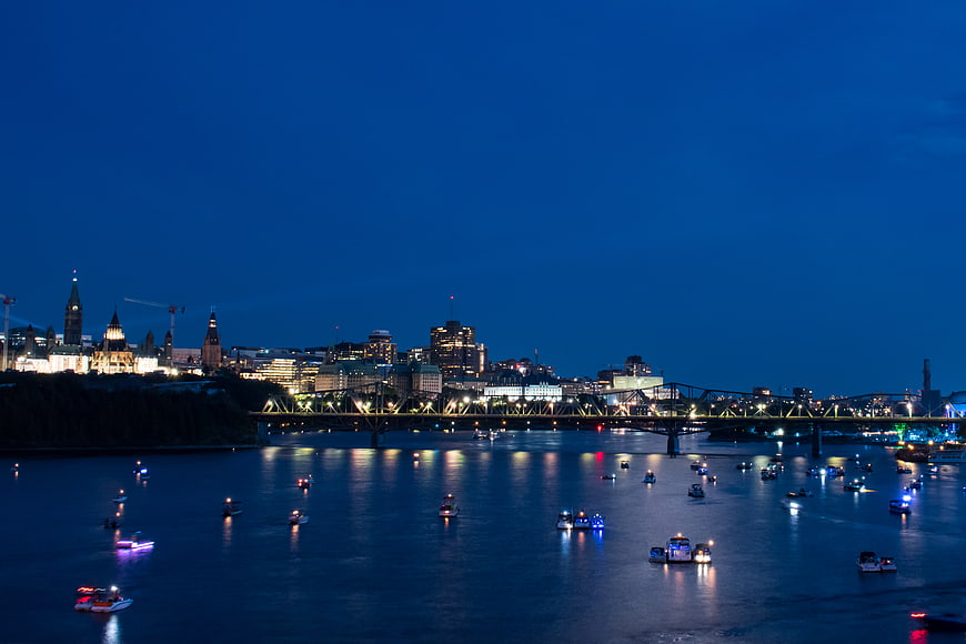 Ottawa skyline at dusk with illuminated Parliament and boats on river