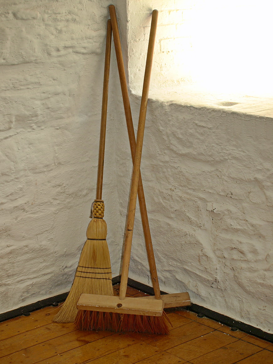 Traditional straw broom and wooden push broom in corner