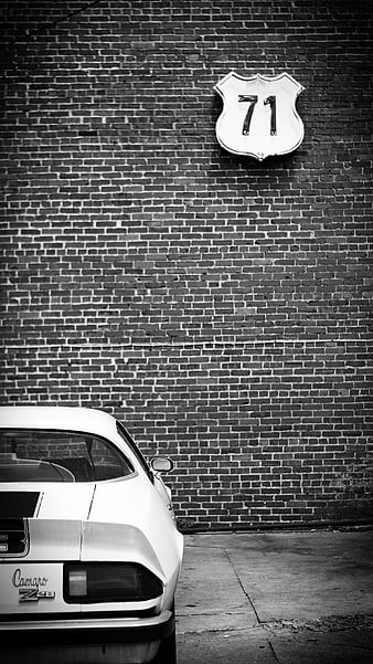 Vintage White Camaro Z28 Parked Against Brick Wall with Route 71 Sign
