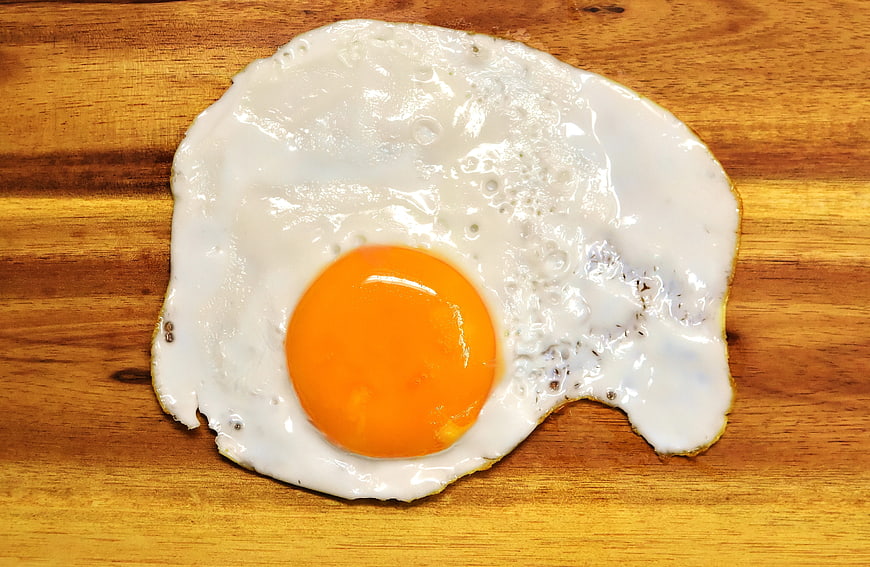 Fried egg with bright yolk on rustic wooden cutting board