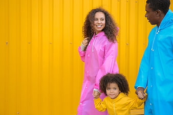 Happy family in colorful raincoats against yellow wall