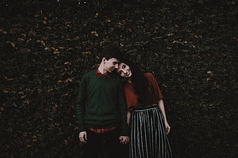 Young couple holding hands against dark hedge background