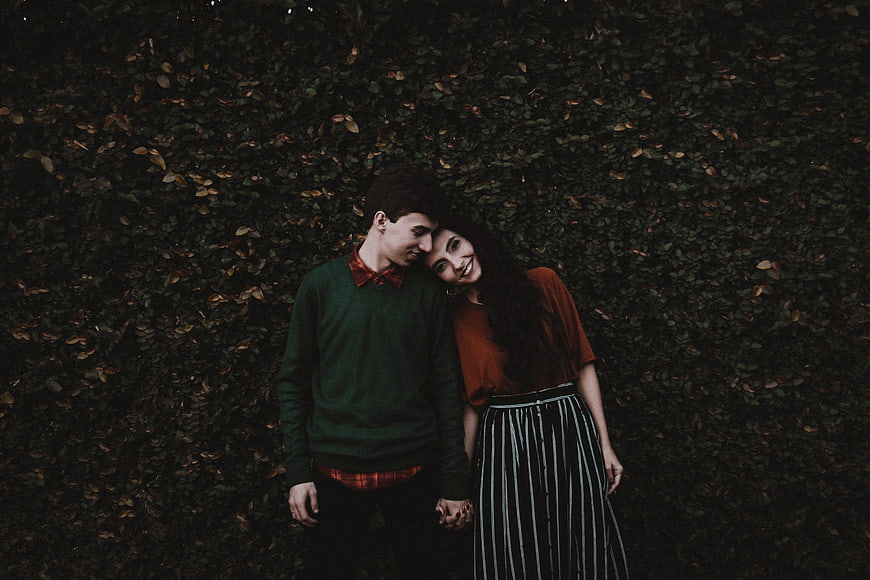 Young couple holding hands against dark hedge background