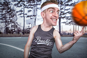 Funny young man spinning basketball on finger outdoors