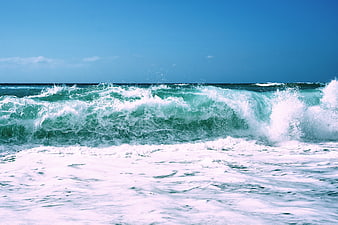 Crashing turquoise ocean waves against a clear blue sky