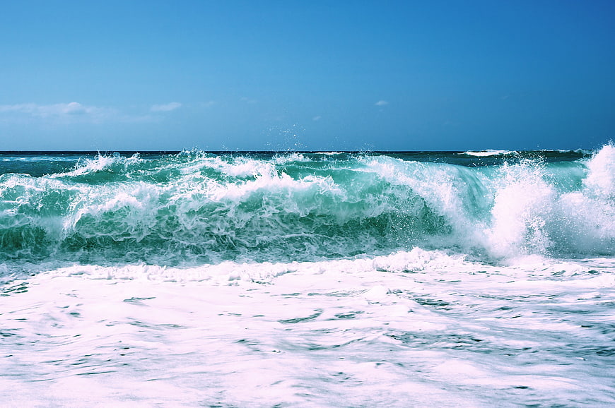Crashing turquoise ocean waves against a clear blue sky