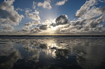 Sun rays through clouds reflecting on wet beach sand