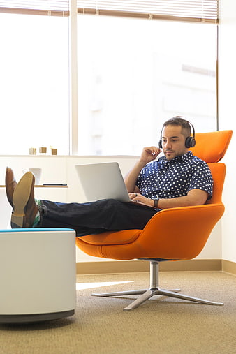 Relaxed man working on laptop in orange office chair