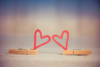 Two wooden clothespins holding red heart cutouts on a blurred background