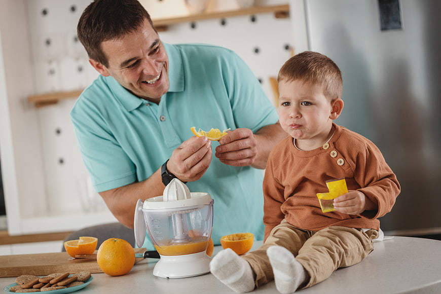 Father and son making fresh orange juice in kitchen