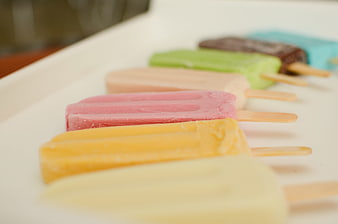 Colorful homemade popsicles arranged in a row on a white surface