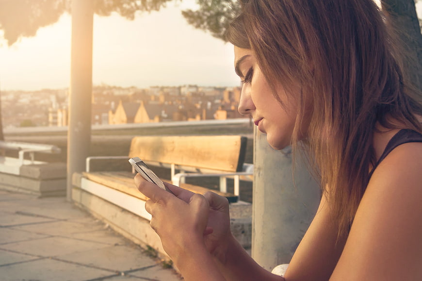 Young Woman Using Smartphone on Outdoor Terrace at Sunset