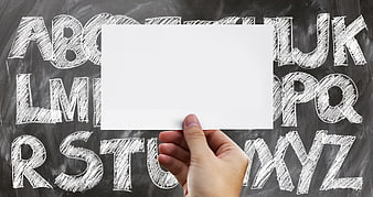 Hand holding blank white card in front of chalkboard alphabet