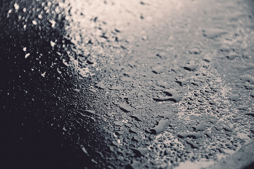 Close-up of water droplets on dark asphalt texture