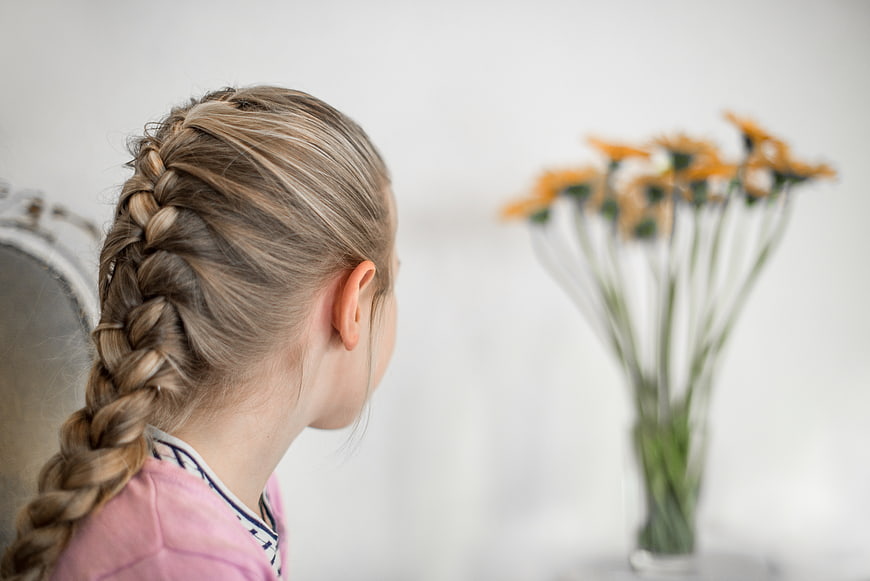 Little girl with braid looking at yellow flowers