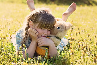 Cute little girl hugging teddy bear in sunny meadow