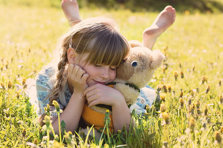 Cute little girl hugging teddy bear in sunny meadow
