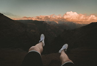 First-person view of legs dangling over a mountain canyon at sunset