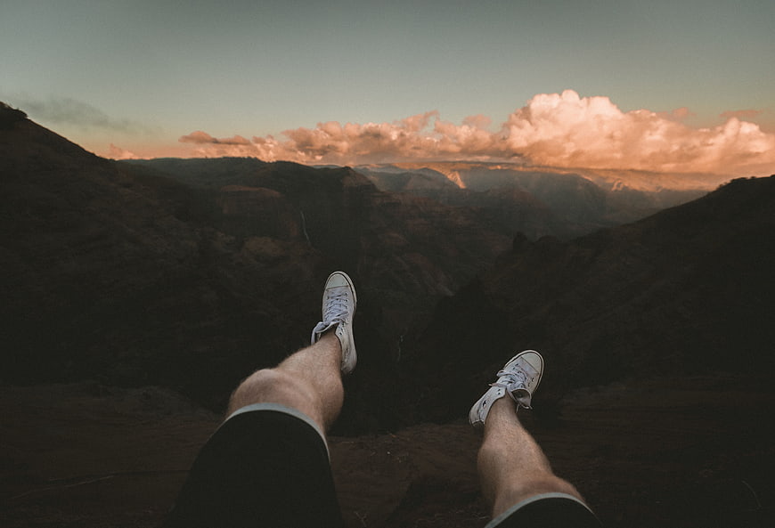 First-person view of legs dangling over a mountain canyon at sunset