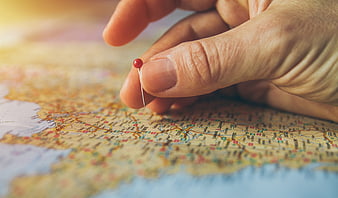 Hand Pinning Red Push Pin on World Map for Travel Planning