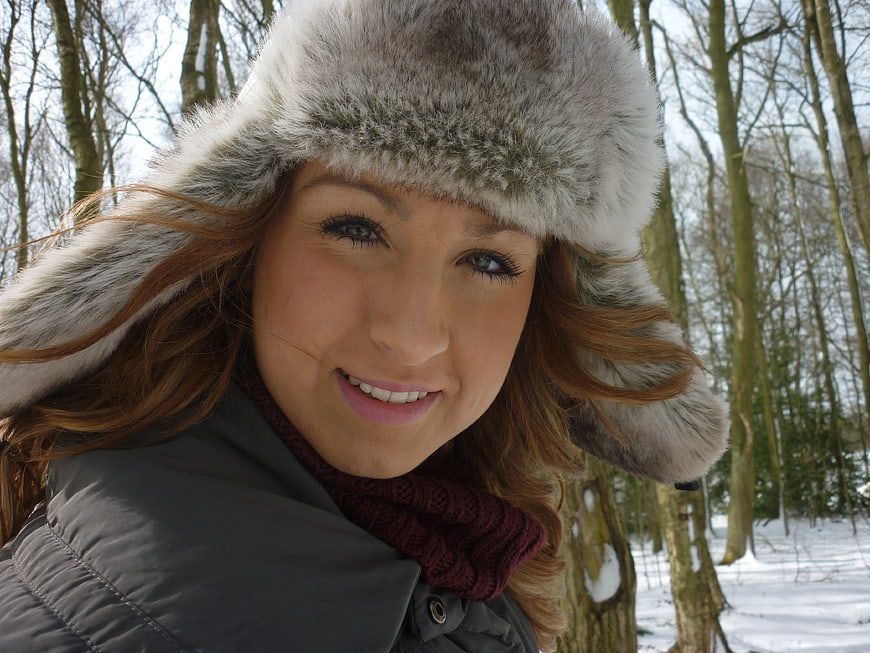 Smiling Woman in Fur Hat in Snowy Winter Forest