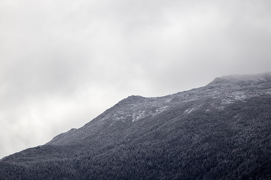 Snow-covered mountain ridge with dense forest and overcast sky
