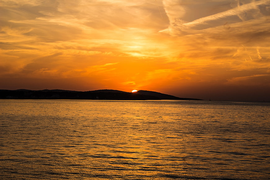 Golden Sunset Over Calm Ocean with Silhouette Hills