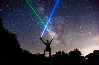 Silhouette of Man Holding Green and Blue Laser Beams Under Milky Way