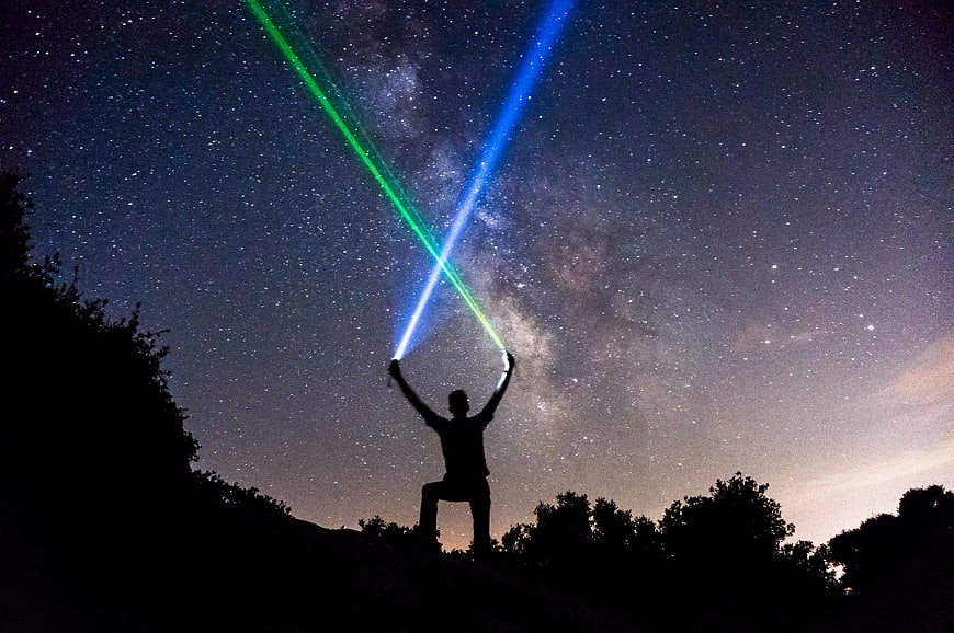 Silhouette of Man Holding Green and Blue Laser Beams Under Milky Way