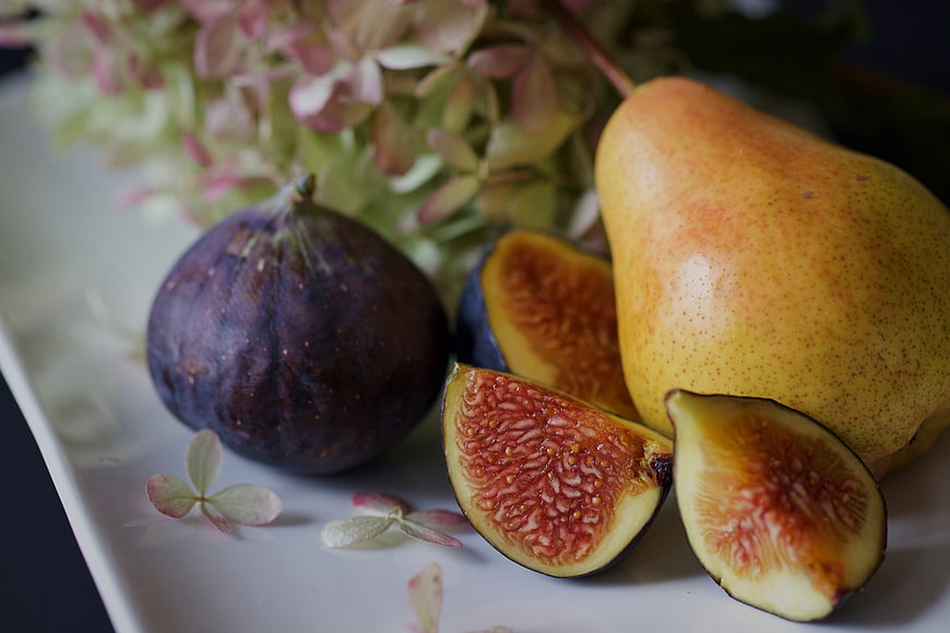 Fresh Figs and Pear on White Plate with Flowers