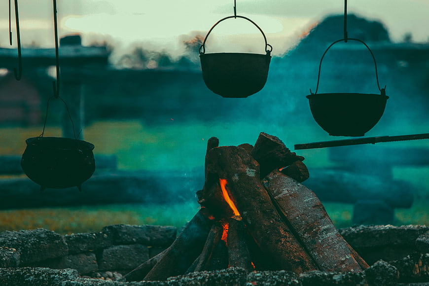 Camping pots hanging over a rustic campfire with smoke