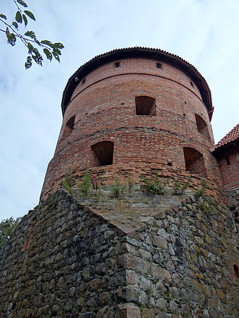 Low angle view of historic red brick castle tower on stone foundation