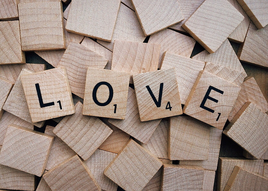 Wooden Scrabble Tiles Spelling Love on Scattered Background