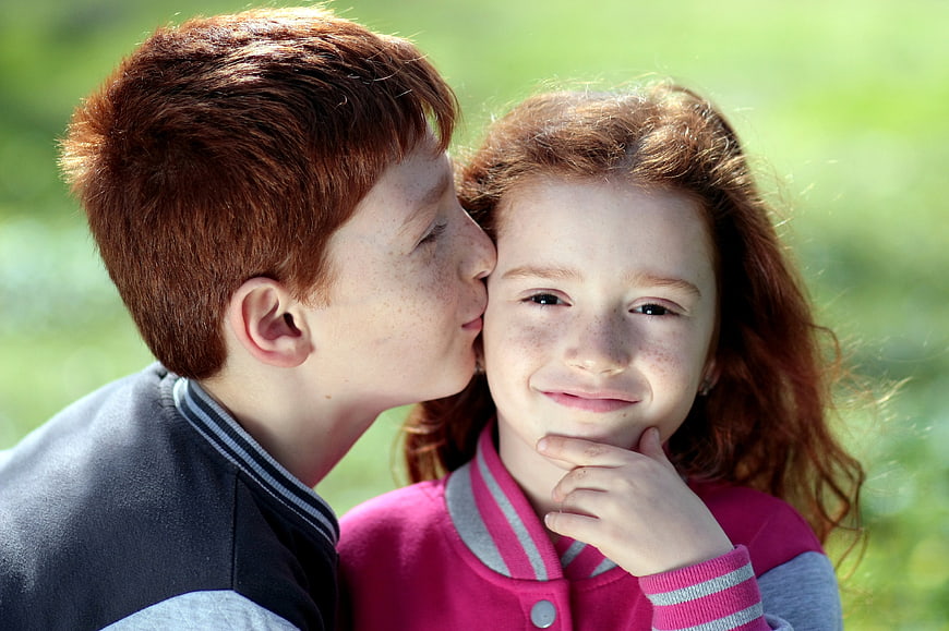 Redhead siblings kissing on cheek outdoors