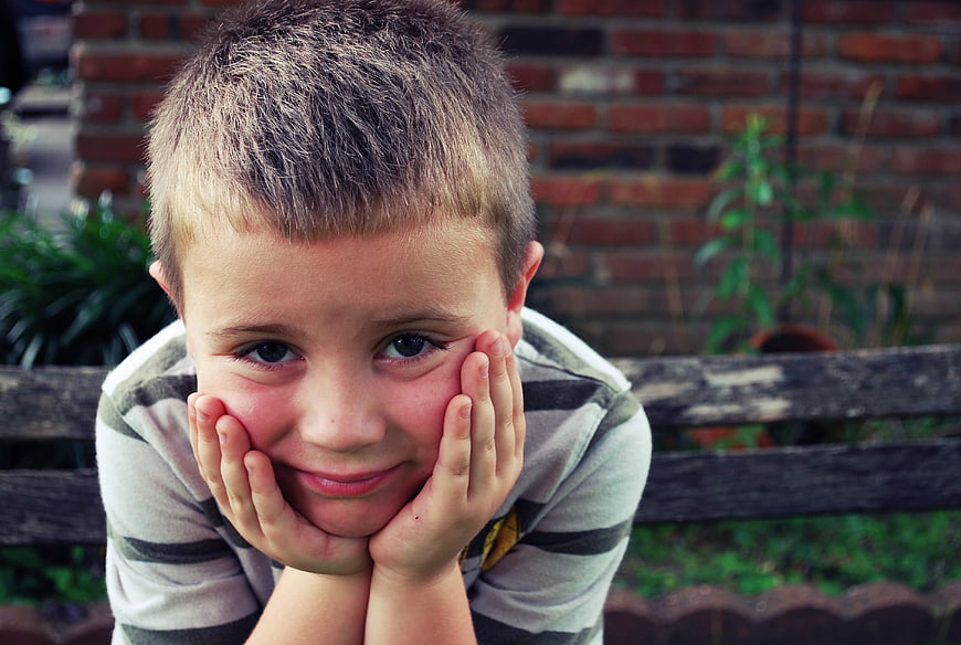 Young boy resting chin on hands with thoughtful expression
