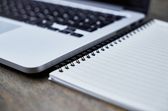 Close-up of silver laptop and spiral notebook on wooden desk
