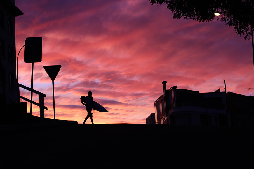 Surfer Silhouette Walking with Board Against Vibrant Sunset Sky