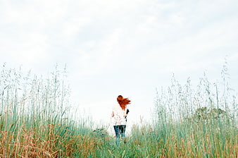 Woman with Red Hair Walking Away in Tall Grass Field