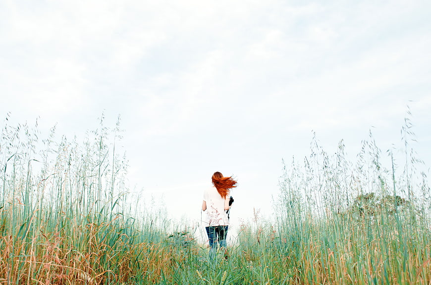 Woman with Red Hair Walking Away in Tall Grass Field