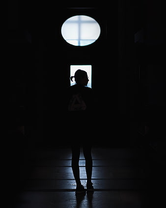 Silhouette of woman standing in dark hallway with light